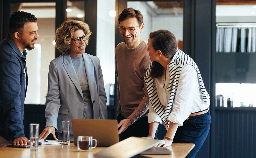 Four people chatting around a laptop in an office environment
